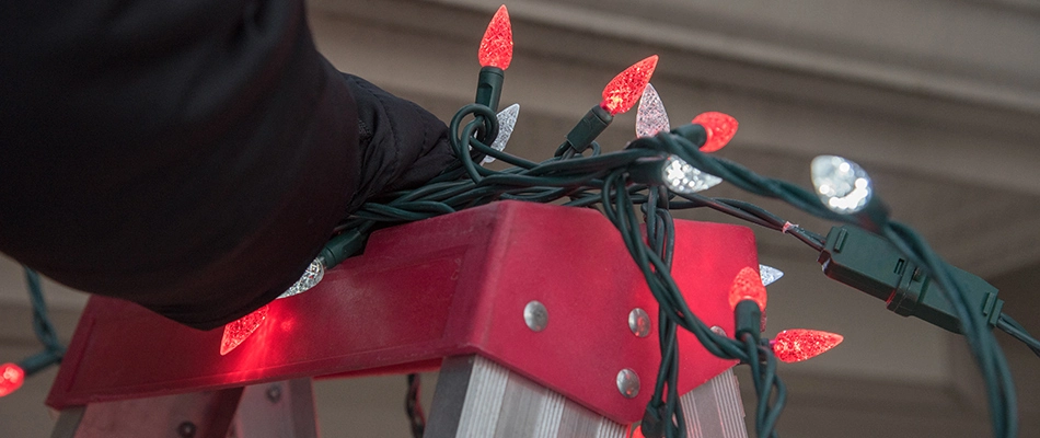 A person stepping on a red ladder to hang holiday lights in Alton, IL.